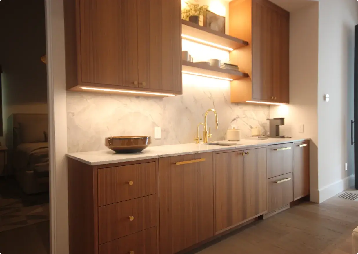 Elegant bar area with warm wooden cabinetry, marble backsplash, and illuminated shelves. A gold faucet and accents add a modern touch to the cozy and stylish space.